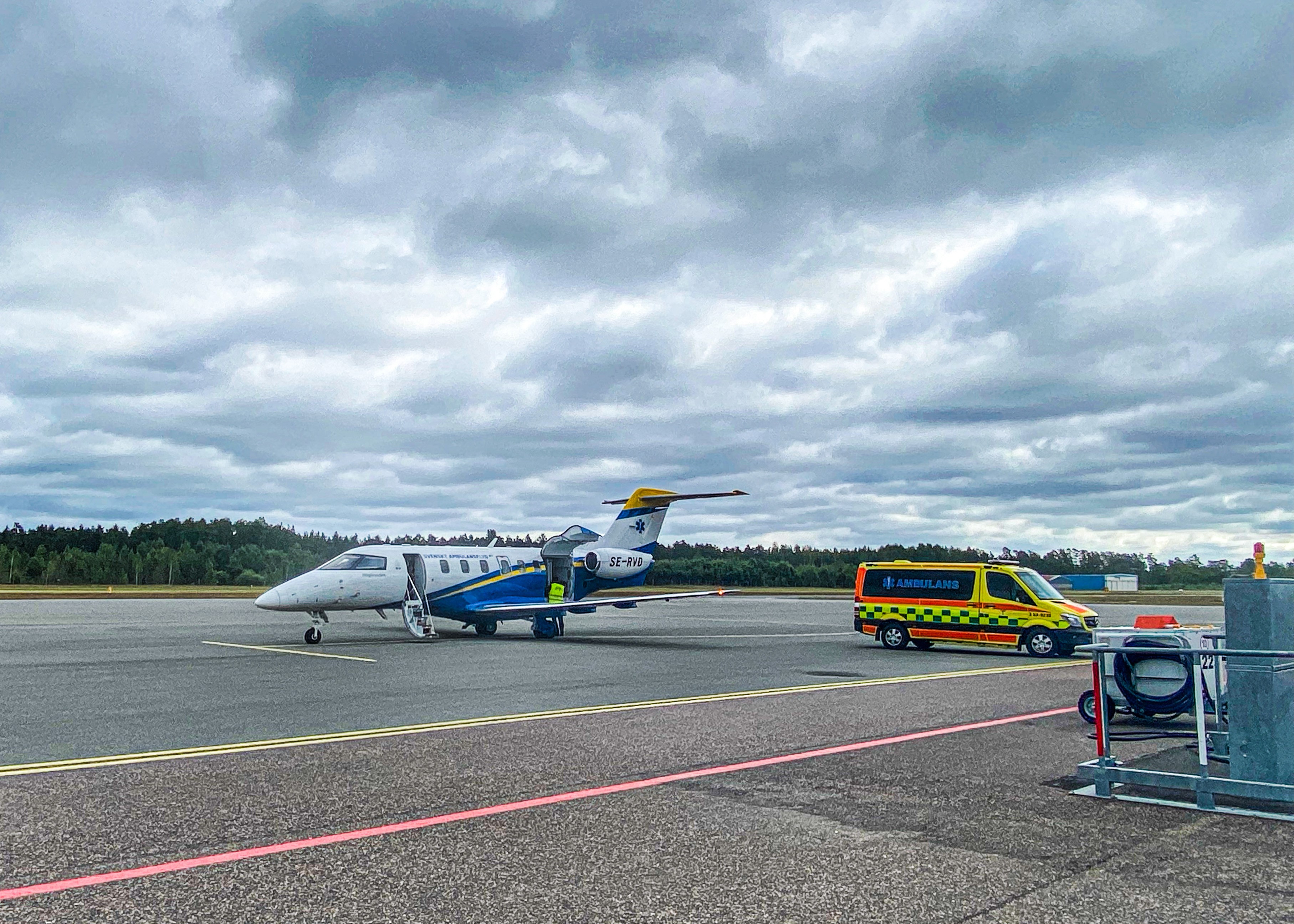 Ambulansflyg parkerat på uppställningsplats. Ambulans uppbackat mot flygplanet för i-/urlastning av patient.