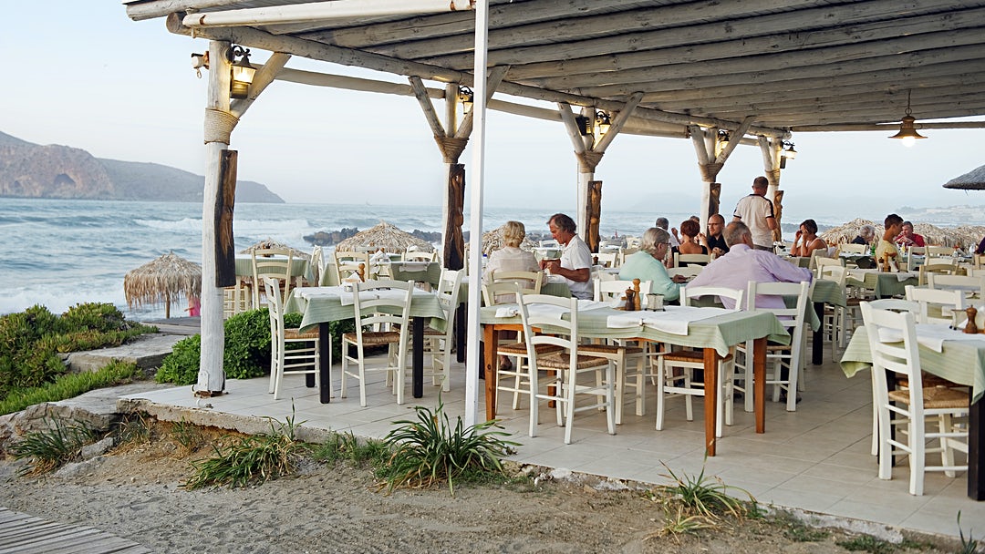 Uteservering på en restaurang i Platanias. Några människor sitter och äter med utsikt ut mot havet.