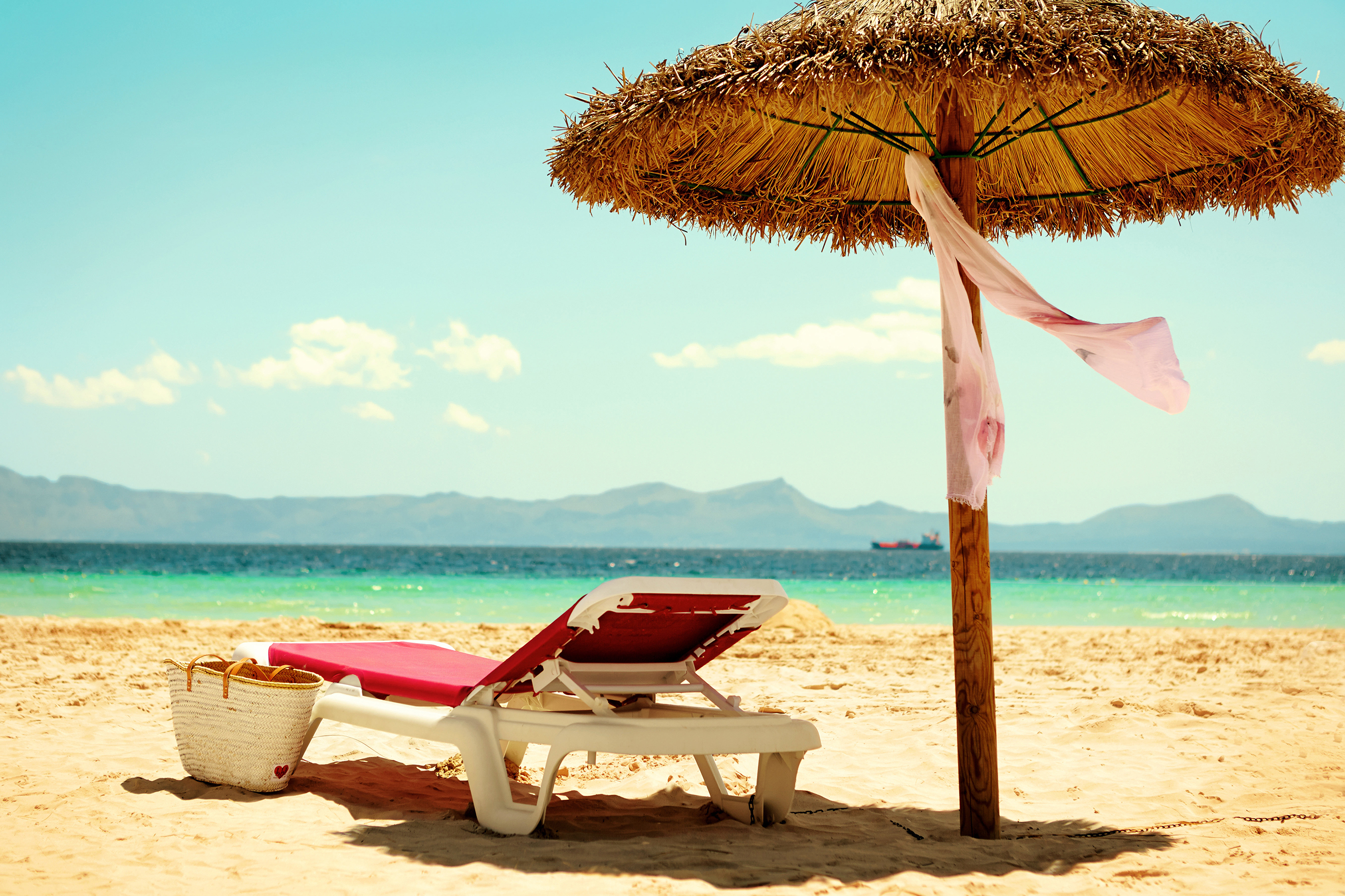 Parasoll och solstol på en tom sandstrand med turkost vatten i bakgrunden