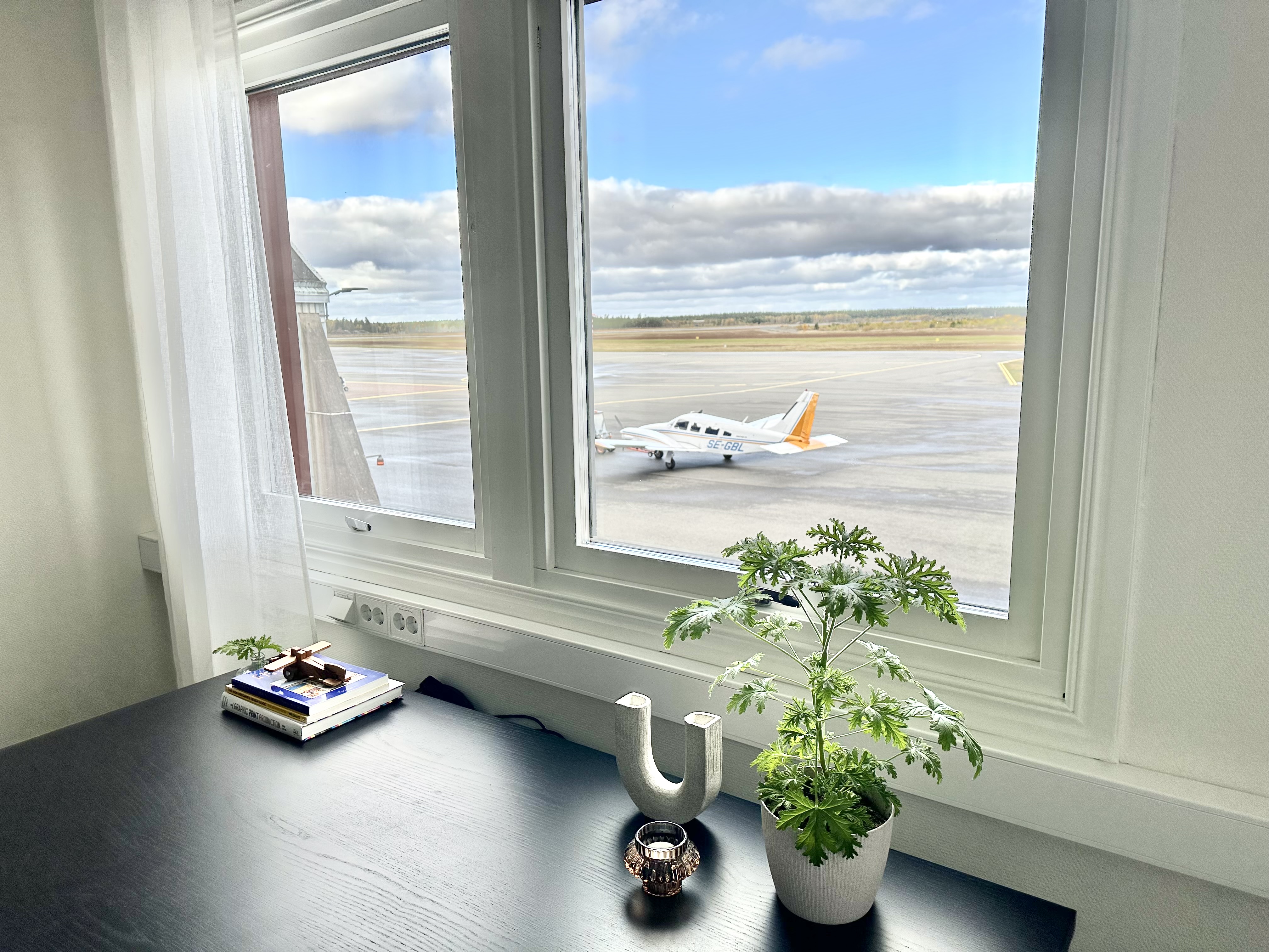 Två kontorsfönster med utsikt över flygplansplattan där det står ett flygplan