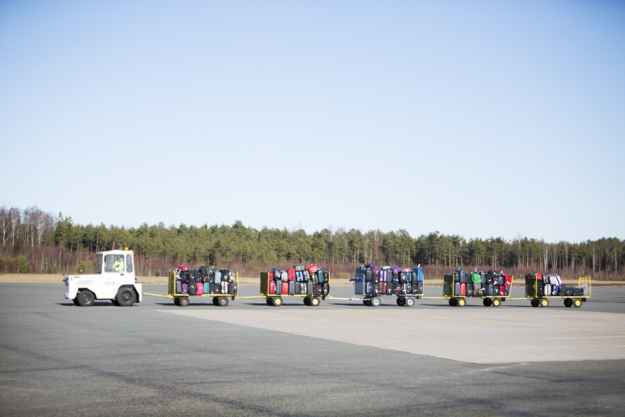 Bagagetruck som kör ett långt tåg med bagagevagnar med väskor